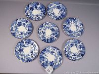 Top-down view of 8 scalloped blue and white Royal Crown Derby Mikado salad plates arranged in a circle showing decorative patterns and no visible damage.
