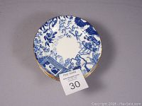 Stack of 8 blue and white scalloped bread and butter plates with gold trim and Asian design, showing lot quantity and condition.