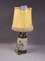 Full view of the antique Asian brass and porcelain table lamp with yellow fabric shade and fringe trim