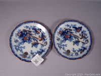Photo of two scalloped Imari cabinet plates with blue floral and architectural design, iron red, and gold accents.
