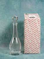 Front view of clear lead crystal decanter with faceted stopper standing beside original Nachtmann branded box.