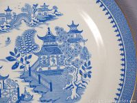 Close-up showing pastoral oriental blue willow pattern with pagodas and boats on the plate's surface.
