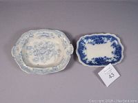 Two ceramic trays side by side on gray surface, larger Asiatic Pheasant style tray with floral motifs on left, smaller flow blue tray on right