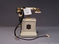 Front view of the white metal base telephone showing brass cradle, Bakelite receiver, and attached cord.