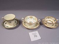 Three Royal Crown Derby porcelain pieces including two soup bowls with saucers and one cup with saucer, showing distinctive patterns and gold trim.
