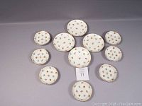Twelve pieces of fine china arranged on gray background showing small fruit bowls, napkin dishes (nappies), and saucers all decorated with small flowers and gold trim.