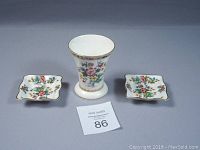 View of the Coalport Ming Rose vase centrally placed between two square butter pads with floral pattern and gold edging.