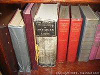 Books on a shelf showing titles including The Complete Encyclopedia of Antiques, Intimate Papers of a Colonial House, and others, with visible wear on the dust jackets and spines.