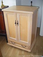 Front view of light wood entertainment unit with two paneled doors and drawer at bottom.