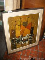 Framed oil on canvas painting showing sailboats with colorful sails and birds flying, placed leaned against a wall.