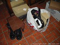 Black steel toe Dr. Martens work boots with long brown leather boots and a large cloth bag filled with assorted bags and shoes.