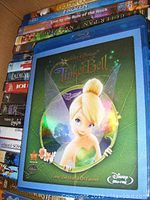 Boxes of DVDs and Blu-rays stacked showing Tinker Bell Blu-ray on top and view of various titles beneath.