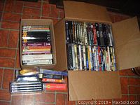 Box sets and DVDs in two cardboard boxes on floor, showing a variety of TV series and DVDs included in the lot