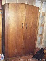 Front view of vintage wooden armoire with closed double doors, showing wood grain and handles.