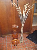 Photo of two-piece solid wood carved vase, wooden bowl, and tall wooden decoration with reed accents against wooden cabinetry and tiled floor.