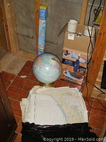 Photo of stacked nautical maps and a world globe on a brass-colored stand on a tiled floor