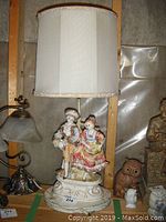 Full view of the decorative table lamp showing painted figurine base and fabric lampshade.