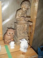Photo showing the child reading statue and three small owl figurines on a wooden shelf within a transparent plastic background.
