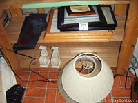 View showing two white carved decorative bookends, several picture frames stacked with 13x16 prints, and a beige pleated lamp shade on floor