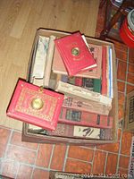 Full top view of one box containing many old books with damaged spines, some with colorful hardcovers including two red elaborate books.