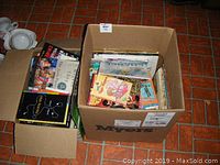 Two cardboard boxes filled with various books including novels and children's books viewed from above with tiled floor background