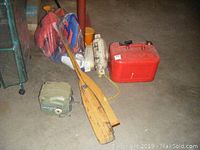 Lot overview showing two wooden paddles, red gas can, white bumpers, adult life jackets in orange and blue, safety kit items and green Powerwinch electric winch on concrete floor.