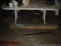 Large white resin rectangular table with slatted top surface and sturdy legs. Shown indoors with several small pots and items on top.
