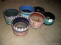 Six planters arranged on floor: four signed multicolor ceramic planters with intricate patterns and two solid Blue Mountain style planters, one blue and one black-green, visible.
