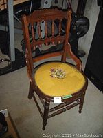 Front view of vintage wooden chair showing the carved backrest spindles and padded needlepoint floral seat.