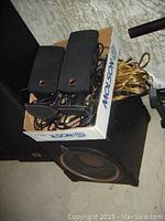 Powered subwoofer with two black rectangular speakers and assorted cables in a box.