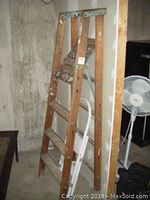 Wooden 4-step ladder leaning against a wall, showing wear and aged wood with metal reinforcements
