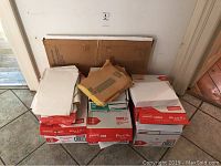 Photo showing stacked unopened Staples white copy paper boxes and envelopes placed on top.