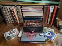 Photo showing a large collection of vinyl LP records stacked vertically and horizontally. Includes jazz LPs and some vintage packaging.