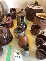 Photo showing seven varied pottery flower vases, a lidded jar, handled jug, cups, and pots in earth toned glazes