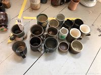 View of 16 assorted pottery mugs and creamers in various earthy glaze colors, showing grouping and relative sizes.