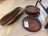Top view showing seven round wooden plates stacked with one long oval wooden tray with a divider on the left side.