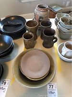 Photo showing 10 pottery items including mugs, plates, bowls, and vases arranged on table
