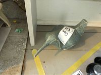 Side view of ceramic bird sculpture showing elongated beak and tail, with pottery tag visible marked 'Pottery'.