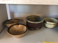Four small bowls including two speckled cream, one with raised pattern, one dark brown bowl, and one bowl with vertical speckled sides.