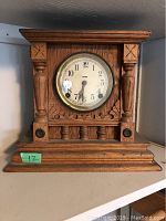Wooden mantel clock front view with carved columns and detailing, Arabic numerals on dial