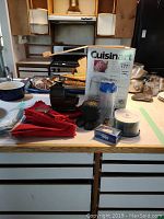 View of all the items on kitchen counter includes the Cuisinart ice cream maker box, red napkins, kitchen timer, CDs in spindle case, and metal knitting ball holder.