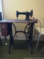 Full view of the Singer sewing machine mounted on a wooden table with iron treadle base.