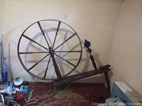 Full view of large antique wooden spinning wheel showing circular wheel, spokes, and base.