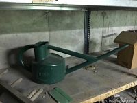 Green plastic Haws watering can on shelf with pipe below