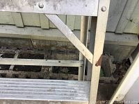 Close-up showing ribbed aluminum steps and side bracing with visible wear and rust spots on the ladder's surface.
