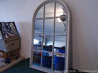 Front view of large arched wall mirror with windowpane design showing reflection of room interior.