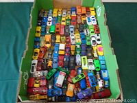 Over 100 assorted die cast cars and trucks arranged in rows inside a box, showing a variety of colors and models.