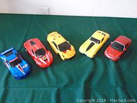 Five assorted large toy cars arranged on green surface. Varied colors include blue, red, yellow. Shows overall condition and size.