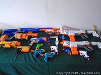 Group photo of all Nerf guns laid out on green fabric background, showing variety and condition.