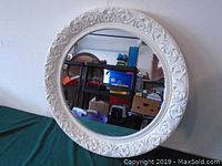 Front view showing the white ornate carved frame around the round mirror surface.